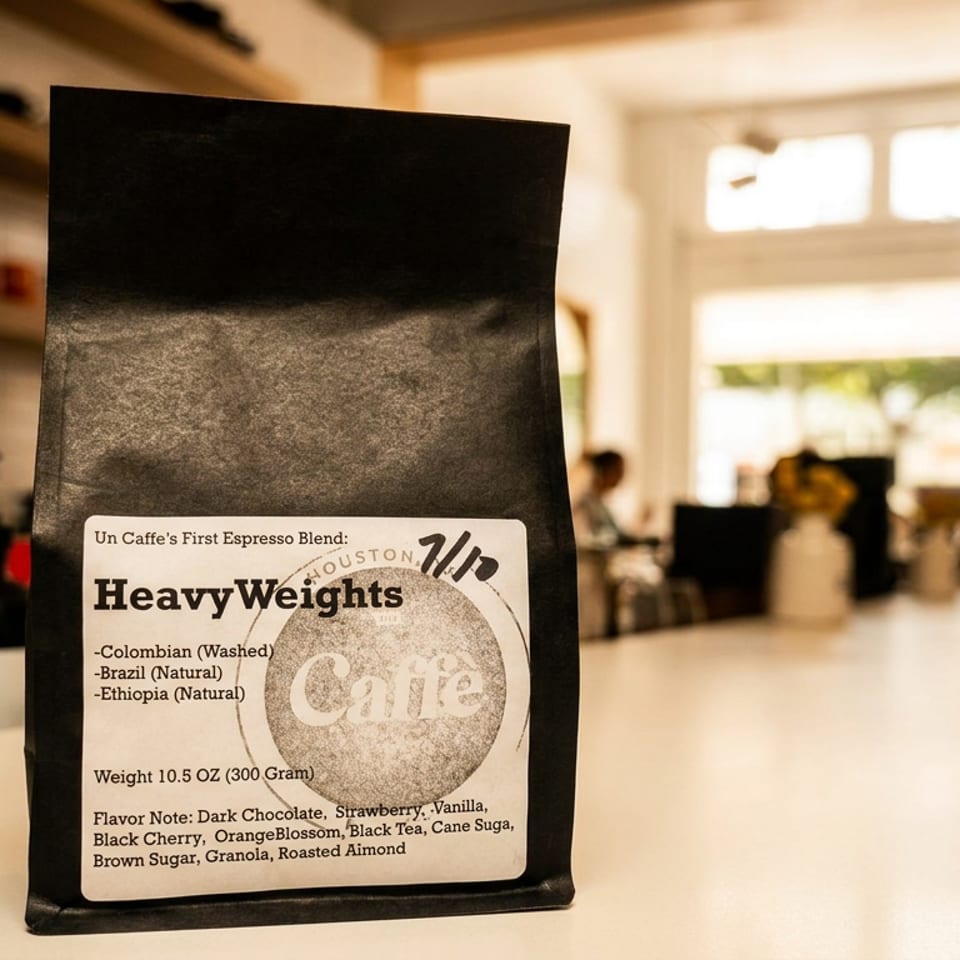 Bag of Heavyweights espresso blend coffee beans displayed on a café counter, with shelves and a softly blurred coffee bar in the background.
